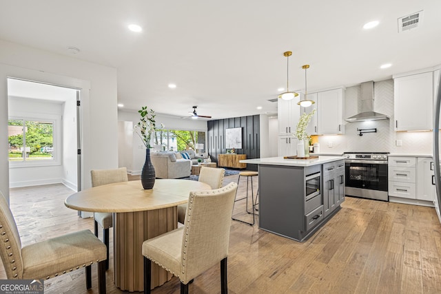 kitchen with white cabinets, wall chimney range hood, appliances with stainless steel finishes, and visible vents