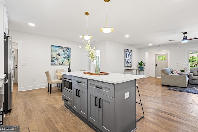 kitchen featuring light countertops, light wood-type flooring, gray cabinetry, a kitchen bar, and appliances with stainless steel finishes