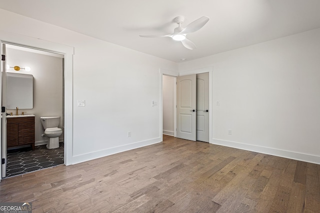 unfurnished bedroom with a sink, ensuite bathroom, baseboards, a ceiling fan, and wood finished floors