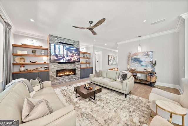 living room featuring crown molding, ceiling fan, recessed lighting, wood finished floors, and a stone fireplace