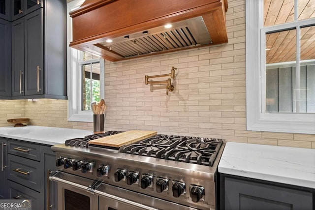 kitchen featuring range hood, light stone countertops, backsplash, double oven range, and gray cabinetry