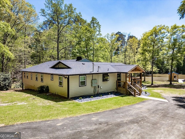 back of property featuring a shingled roof, a chimney, a yard, and stairway