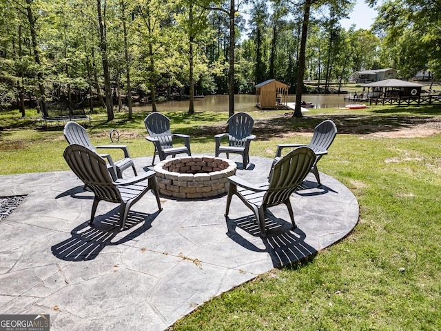 view of patio with a trampoline, a shed, an outbuilding, a water view, and a fire pit