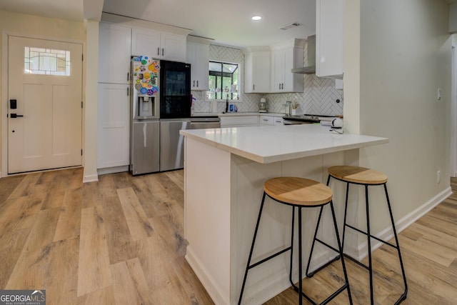 kitchen featuring wall chimney range hood, a kitchen bar, appliances with stainless steel finishes, a peninsula, and white cabinetry