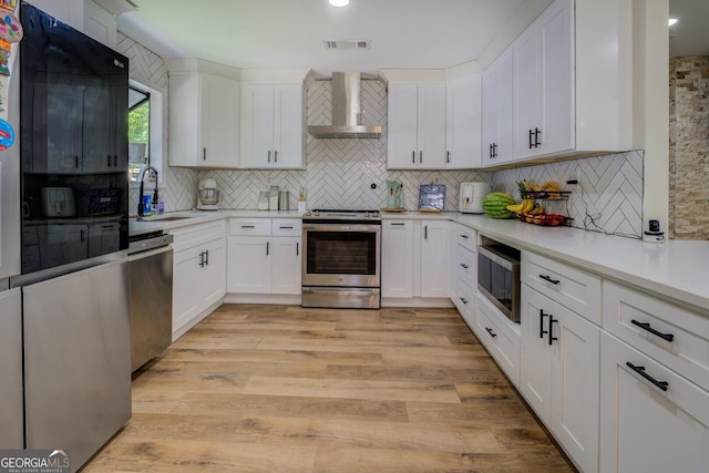 kitchen featuring wall chimney range hood, a sink, stainless steel appliances, backsplash, and visible vents