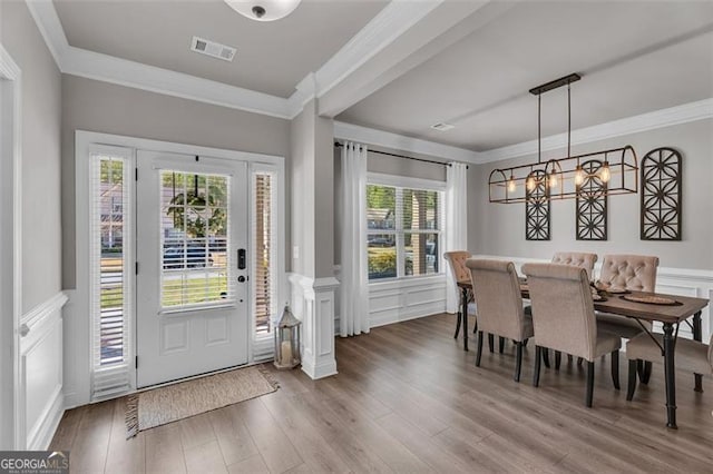 entrance foyer with a decorative wall, visible vents, ornamental molding, and wood finished floors