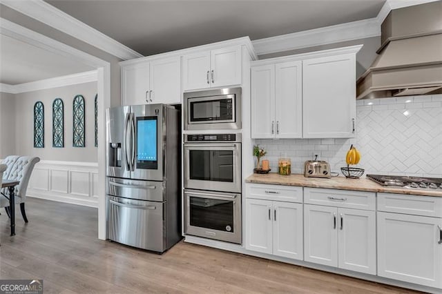 kitchen featuring stainless steel appliances, custom exhaust hood, white cabinetry, and crown molding