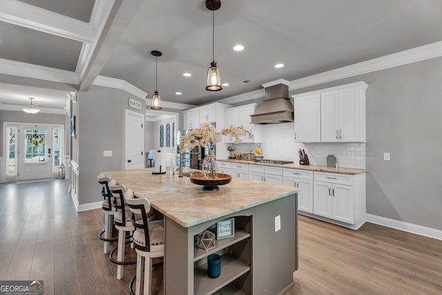 kitchen featuring custom range hood, baseboards, light wood-type flooring, crown molding, and stainless steel gas cooktop