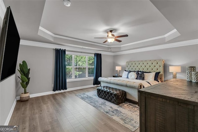 bedroom featuring a tray ceiling, wood finished floors, baseboards, and ornamental molding