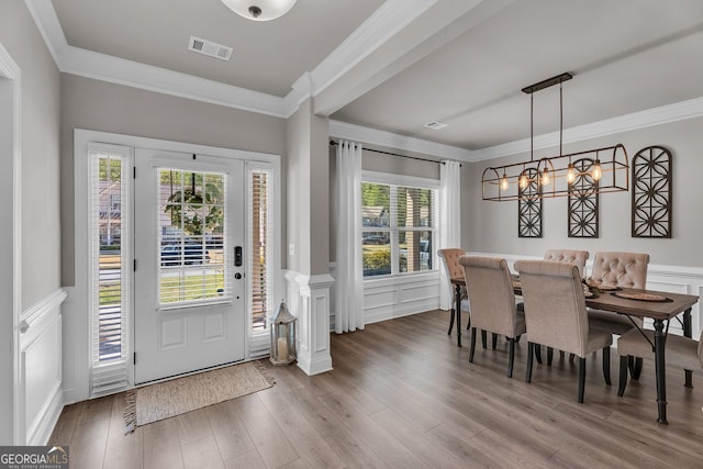 foyer featuring visible vents, a decorative wall, ornamental molding, wainscoting, and wood finished floors