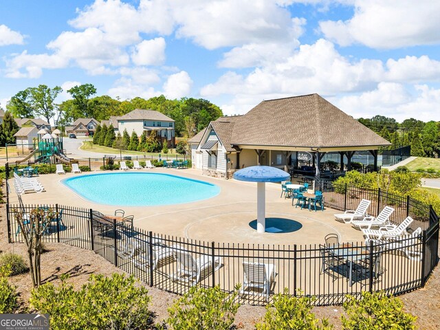 community pool with a patio area, fence, and playground community