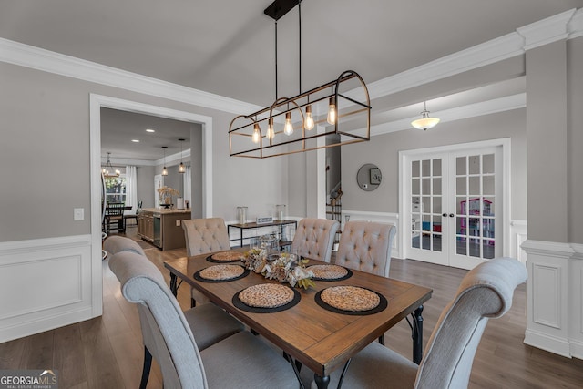 dining room featuring dark wood-style flooring, ornamental molding, a chandelier, french doors, and wainscoting