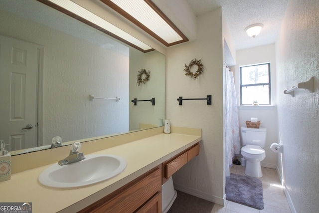 full bathroom with vanity, toilet, tile patterned floors, a textured wall, and baseboards