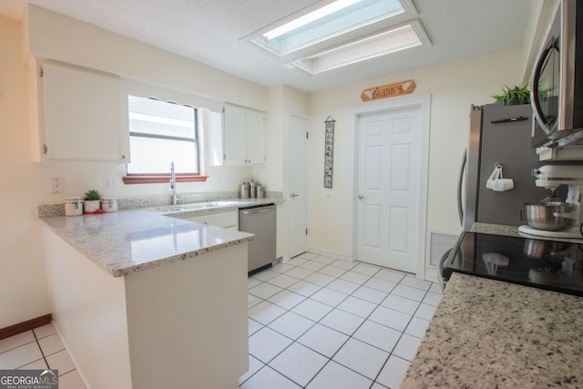 kitchen with light tile patterned floors, a peninsula, white cabinetry, a sink, and stainless steel appliances