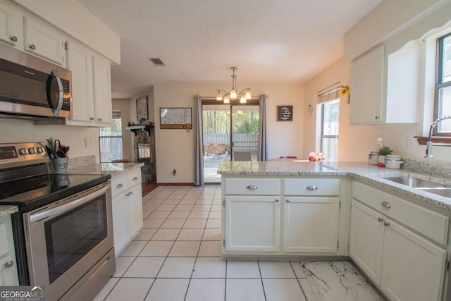 kitchen with a peninsula, visible vents, appliances with stainless steel finishes, a sink, and a notable chandelier