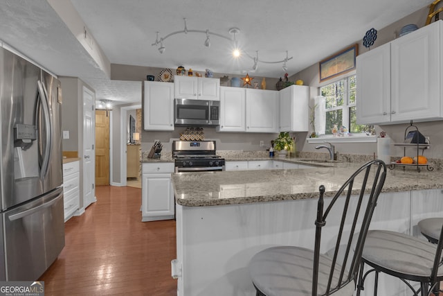 kitchen featuring a peninsula, appliances with stainless steel finishes, white cabinets, and a sink