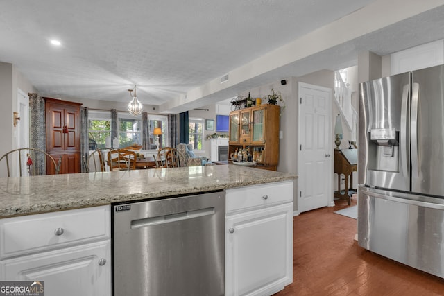 kitchen with a textured ceiling, a notable chandelier, white cabinets, and appliances with stainless steel finishes