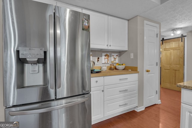 kitchen featuring stainless steel fridge with ice dispenser, white cabinets, a barn door, and wood finished floors