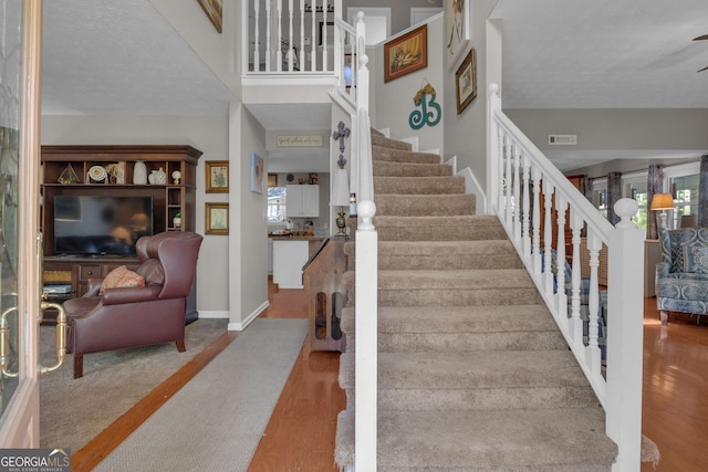 staircase with baseboards, visible vents, a textured ceiling, and wood finished floors