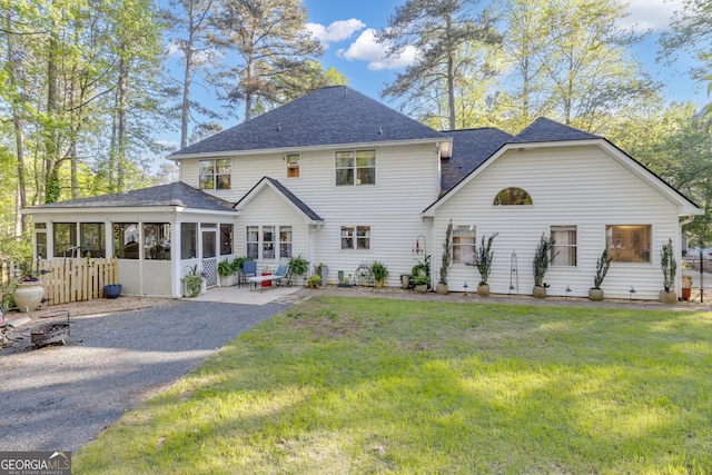 rear view of property featuring roof with shingles, a sunroom, and a lawn