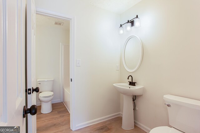 bathroom featuring toilet, wood finished floors, baseboards, and visible vents