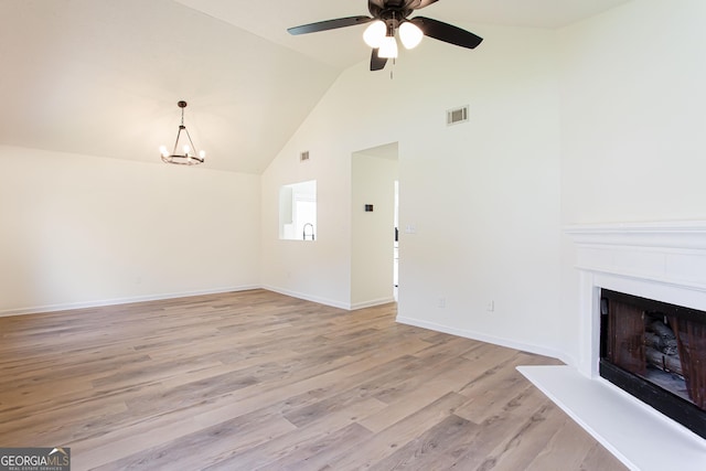 unfurnished living room with a fireplace with raised hearth, visible vents, high vaulted ceiling, light wood finished floors, and ceiling fan with notable chandelier