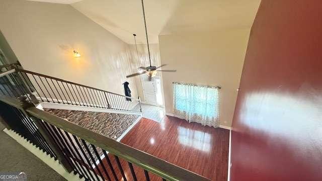 stairway featuring baseboards, a ceiling fan, high vaulted ceiling, and wood finished floors