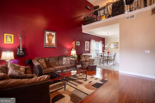 living area with a towering ceiling, crown molding, visible vents, hardwood / wood-style flooring, and baseboards