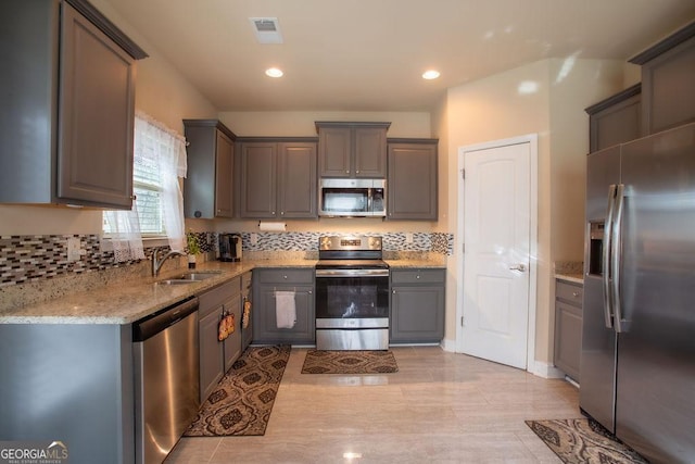 kitchen featuring visible vents, light stone countertops, gray cabinetry, a sink, and stainless steel appliances