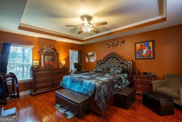 bedroom with crown molding, dark wood-style flooring, ceiling fan, a tray ceiling, and visible vents