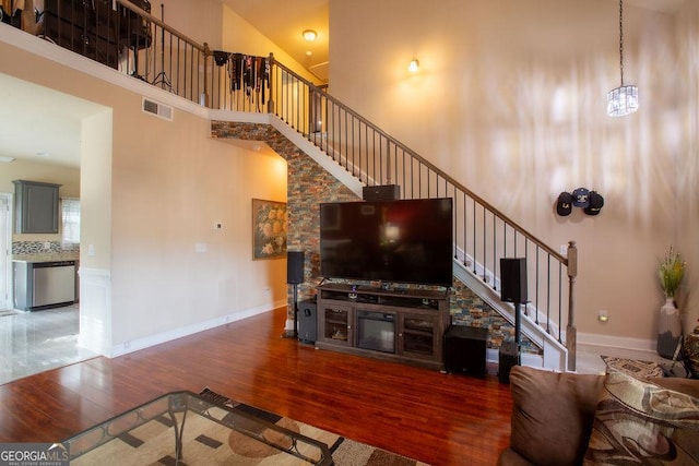 living room with visible vents, a towering ceiling, wood finished floors, baseboards, and stairway