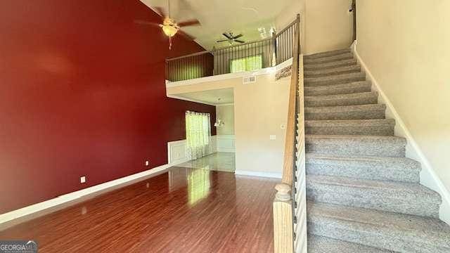 stairs with wood finished floors, a ceiling fan, baseboards, and a high ceiling