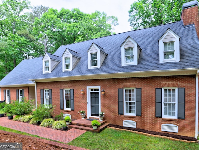 new england style home featuring brick siding, a shingled roof, and a chimney