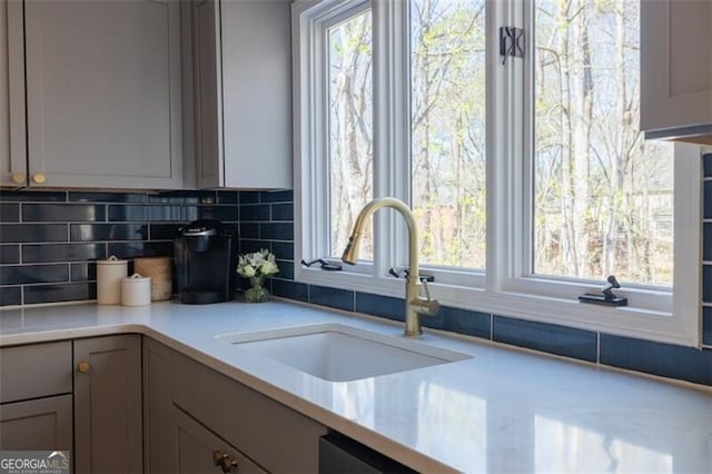 kitchen with a sink, backsplash, light countertops, and healthy amount of natural light