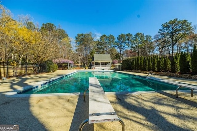 view of pool featuring a diving board, fence, a patio area, and view of wooded area