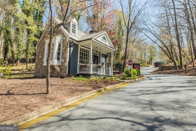 view of side of home with a porch, stone siding, and driveway