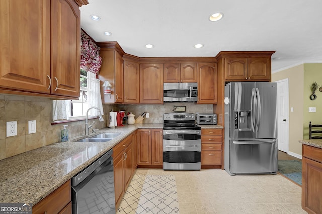 kitchen featuring appliances with stainless steel finishes, a sink, light stone countertops, brown cabinetry, and recessed lighting