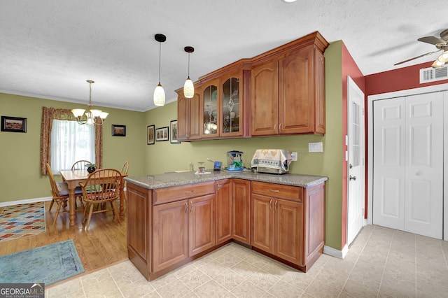 kitchen featuring brown cabinetry, a textured ceiling, glass insert cabinets, a peninsula, and ceiling fan