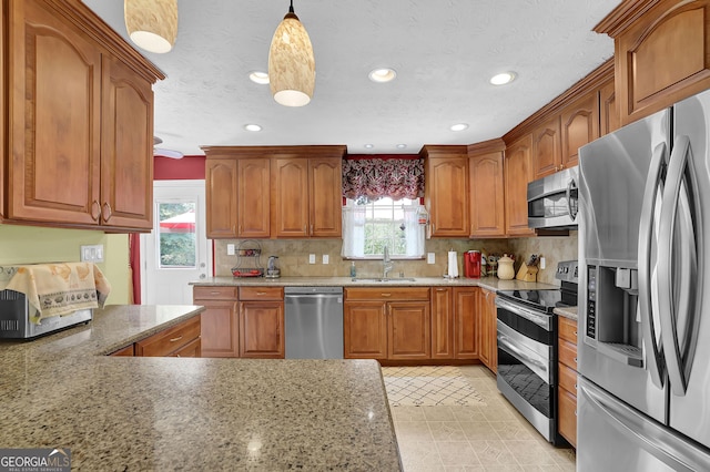 kitchen featuring stainless steel appliances, a sink, brown cabinets, decorative backsplash, and recessed lighting