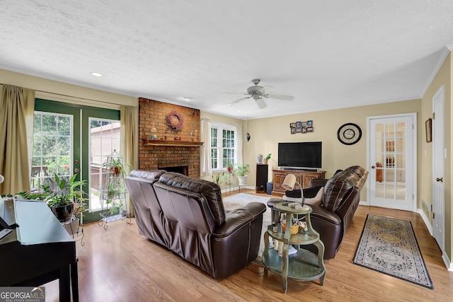 living room featuring wood finished floors, ceiling fan, a textured ceiling, a fireplace, and baseboards