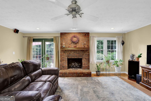 living room with wood finished floors, a ceiling fan, ornamental molding, a fireplace, and a textured ceiling
