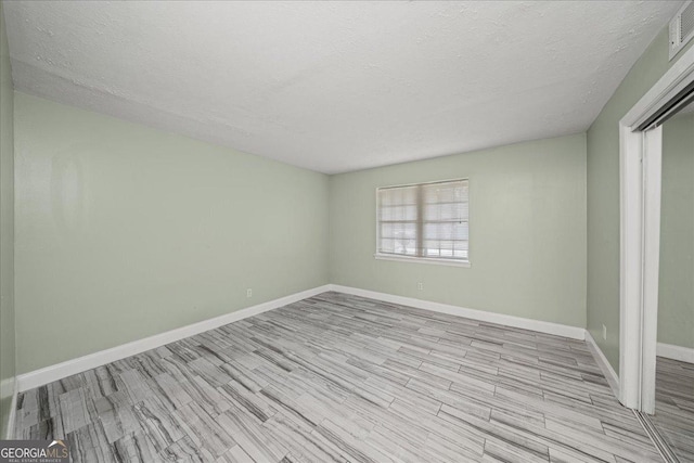 empty room with baseboards, wood finished floors, and a textured ceiling