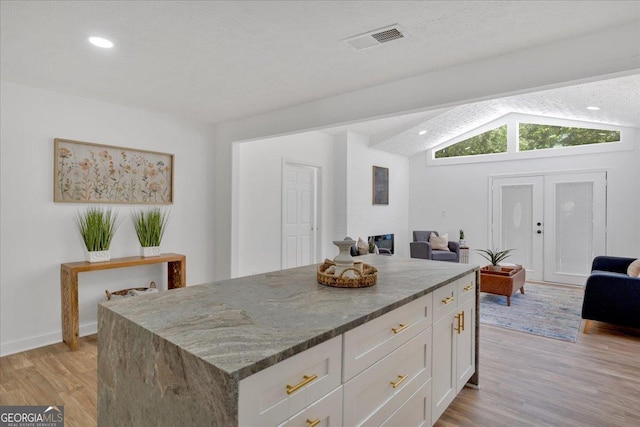 kitchen with light wood-type flooring, stone counters, visible vents, white cabinetry, and lofted ceiling