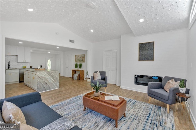 living area featuring lofted ceiling, light wood-style flooring, a glass covered fireplace, and a textured ceiling