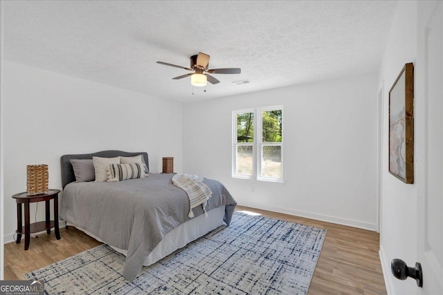 bedroom with a textured ceiling, light wood-type flooring, ceiling fan, baseboards, and visible vents