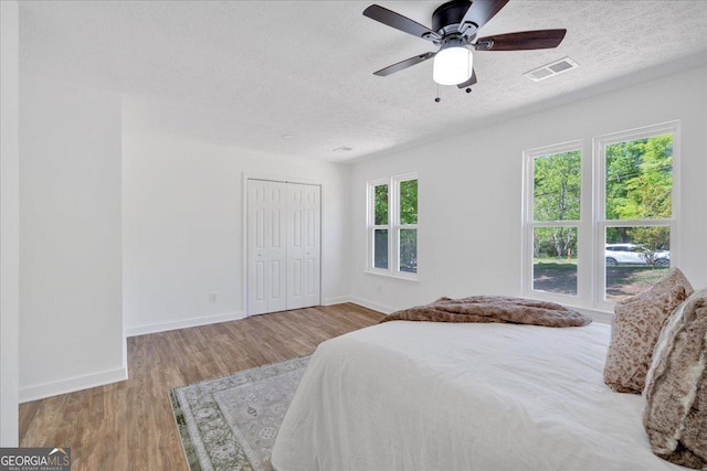 bedroom with wood finished floors, visible vents, a closet, baseboards, and a textured ceiling