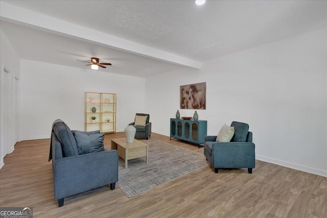 living room with ceiling fan, baseboards, beam ceiling, and light wood-type flooring