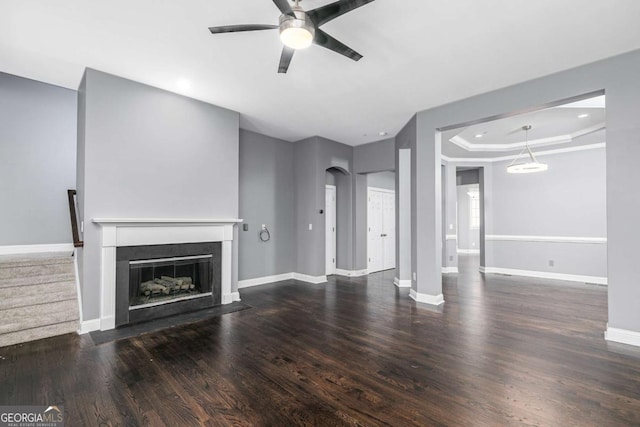 unfurnished living room featuring baseboards, a raised ceiling, a fireplace with flush hearth, ceiling fan, and wood finished floors