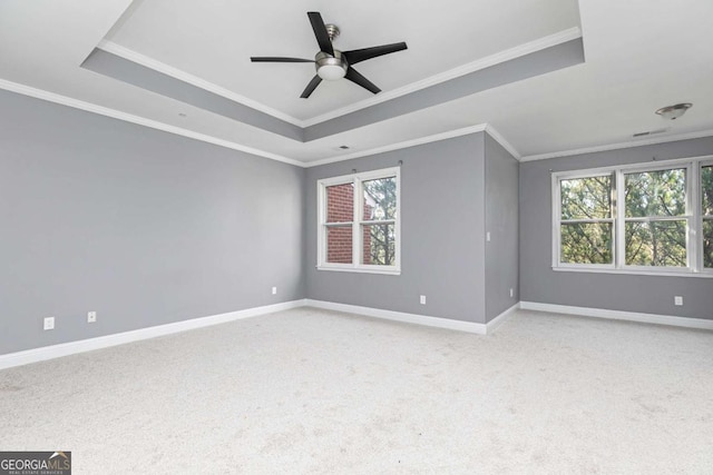 carpeted empty room with baseboards, ornamental molding, a ceiling fan, visible vents, and a tray ceiling