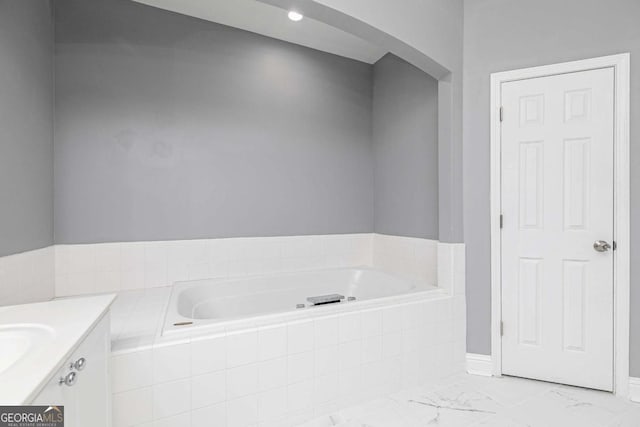 bathroom with marble finish floor, vanity, and a garden tub